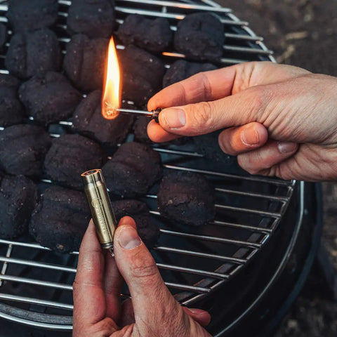 Relightable Bullet Fire Starter Keychain Lighter for Camping and Grilling used to ignite coal briquettes on a grill