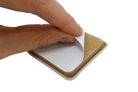 Hand peeling adhesive backing from No Sweat Top Tier 2 Inch Square Furniture Sliders with beige polyethylene glide.