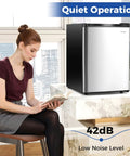 Compact Upright Freezer Featuring Tunable Thermostat And Snap Out Shelves in silver under a counter with a woman reading.