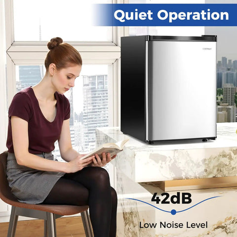 Compact Upright Freezer Featuring Tunable Thermostat And Snap Out Shelves in silver under a counter with a woman reading.