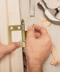 Hands installing vintage style solid metal cabinet door hinge 19mm non mortise folding hinge on wooden surface with tools nearby