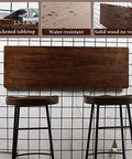 Folding Wall Desk With Solid Wood Board And Two Iron Brackets, 2.8cm Thick, Your Go-To Space Saver For Home Office Or Cafe, Up To 40kg, 120x35cm 47.2x13.8in, Easy Drop Down Design displayed with two stools against a tiled wall.