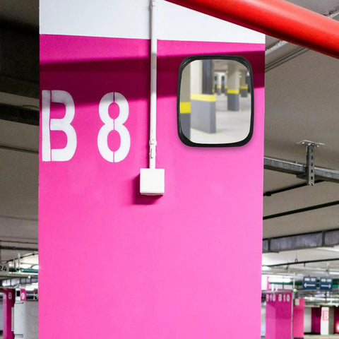 Wide Angle Safety Convex Mirror Rock Solid Wall Mount For Garage Warehouse Parking Lot Crushes Blind Spots And Keeps You Covered With No Fuss Easy Install Setup mounted on pink wall in parking garage.