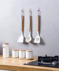 Front view of three clear wall hooks holding wooden-handled kitchen utensils in a row.