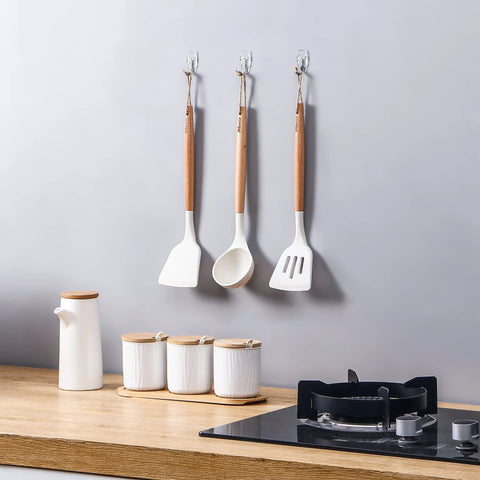 Front view of three clear wall hooks holding wooden-handled kitchen utensils in a row.