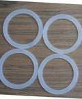 Four white silicone gaskets from Silicone Gasket Replacement Set 10 Pieces For Coffee Pot Lids And Jar Seals on wooden surface.