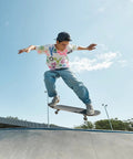 Person skateboarding mid-air in casual attire at a skatepark on a sunny day.