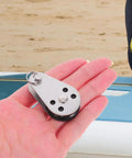 Person holding Beefy Stainless Steel Marine Pulley Kit For Kayaks And Canoes, small wheel design for fishing kayaks