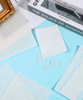Anti Slip Silicone Pads For Glass Tables With 132 Pcs Adhesive Dots and Grippers near books and frame on blue surface