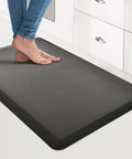 Anti Fatigue Floor Mat Half Inch Cushioned For Kitchen And Standing Desk Non Slip Cushion With ComfortGrip Ideal For Home Office Or Garage Floor 17.3 By 28 Inches Black in use by feet in kitchen setting.