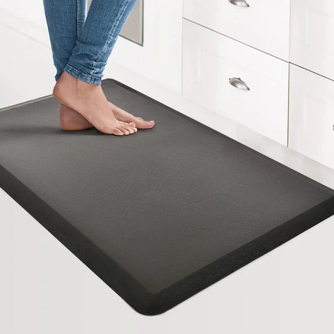 Anti Fatigue Floor Mat Half Inch Cushioned For Kitchen And Standing Desk Non Slip Cushion With ComfortGrip Ideal For Home Office Or Garage Floor 17.3 By 28 Inches Black in use by feet in kitchen setting.