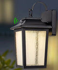 Black metal dusk to dawn outdoor wall light lantern with photocell sensor, mounted on wall, illuminated, 3000K LED light