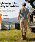 Man carrying folded grill table with mesh desktop for camping and outdoor use, standing by car with camping gear