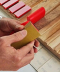 Close-up of person using All-In-One 16-Piece Hook And Loop Sanding Block Kit With 40 Sandpaper Sheets on wood surface