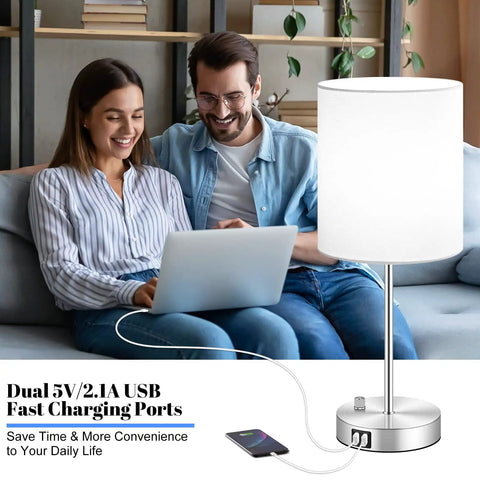 Dual USB Table Lamps With AC Outlet And Rotary Switch, White Fabric Shade Modern Nightstand Lights For Bedroom Living Room And Office, Set Of 2 That Charge Three Devices At Once, shown next to a couple using electronic devices