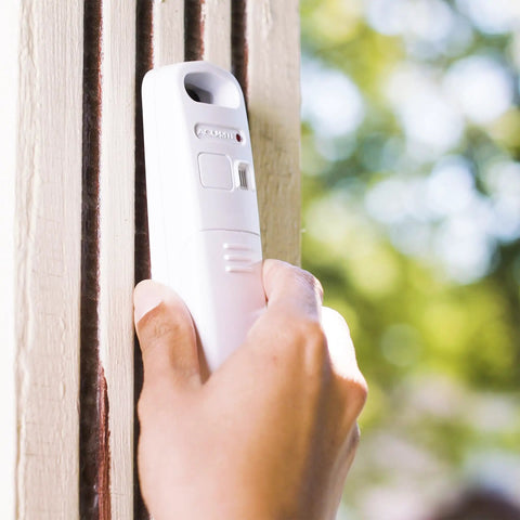 Hand holding a white handheld weather forecaster alarm clock with wireless Qi charging pad showing real-time temperature and humidity