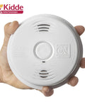 Dual Hazard Smoke And Carbon Monoxide Detector With Voice Warning Hardwired Setup And Ten Year Sealed Lithium Battery Backup Interconnectable Network Built Tough For Zero Drama Family Safety White held in hand.