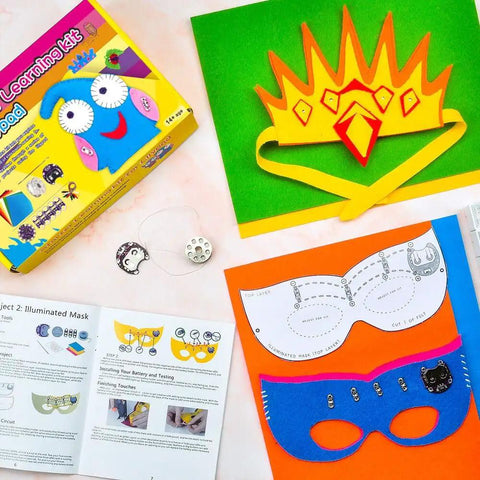 LilyPad Sewable Electronics Starter Kit with colorful mask templates, USB board, and instruction booklet on table.