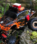 Orange and black RC car on rocks with accessories, showcasing the Beefy One Tenth RC Scale ABS Fuel Tank For Axial Wraith SCX10 Exo AX10 Trucks Pack Of 2 Replace Your Rig With A Sturdy ABS Tank For A Realistic Look Plug And Play Fit Durable Upgrade For Your RC Crawling Beast.