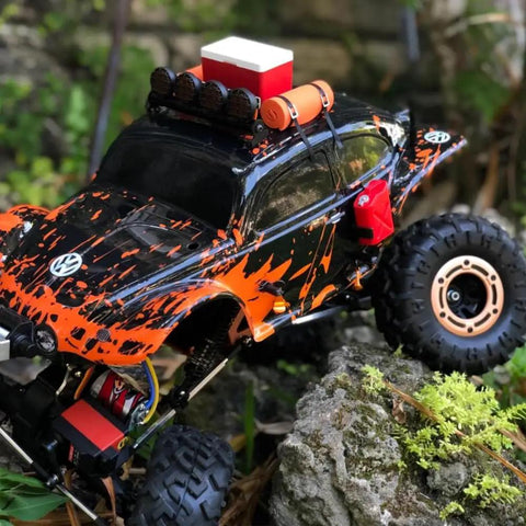 Orange and black RC car on rocks with accessories, showcasing the Beefy One Tenth RC Scale ABS Fuel Tank For Axial Wraith SCX10 Exo AX10 Trucks Pack Of 2 Replace Your Rig With A Sturdy ABS Tank For A Realistic Look Plug And Play Fit Durable Upgrade For Your RC Crawling Beast.