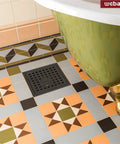 Floor view showing a 6 Inch Square Shower Floor Drain With Flange And Removable Grate Matte Black Stainless Steel SUS 304 Watermark And CUPC Certified Easy Install Clog Resistant Drainage For Fast Water Removal In Standard No Hub Base next to a green bathtub on patterned tiles.