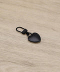 Two Piece Black Heart Shaped Zipper Pull Replacement Kit For Luggage Backpacks Jackets Coats Boots And Clothing Durable Metal Zipper Pulls With Universal Fit For Quick Slider Fix And Easy DIY Repair shown on wooden surface