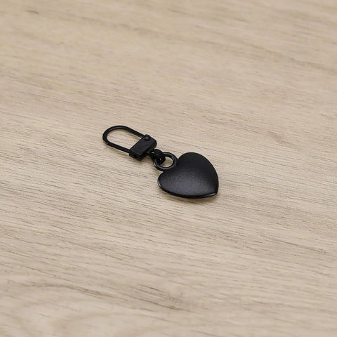 Two Piece Black Heart Shaped Zipper Pull Replacement Kit For Luggage Backpacks Jackets Coats Boots And Clothing Durable Metal Zipper Pulls With Universal Fit For Quick Slider Fix And Easy DIY Repair shown on wooden surface