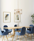 Gold Drum Pendant Light Fixture hanging over wooden dining table with blue chairs in modern dining room.