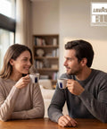Man and woman enjoying coffee from Lavazza Blue cups at home, with warm interior setting and branded logo in view.
