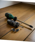Heavy Duty 4 Pc Set Black Mechanical Spring Pins With Wear Resistance For Industrial Workshop Use And Reliable Smooth Operation Plus Super Stable Reset Power On Locating Pins To Keep Your Setup Rock Solid No Drift Amidst Vibration Ever next to a green screwdriver and drill on wooden floor.