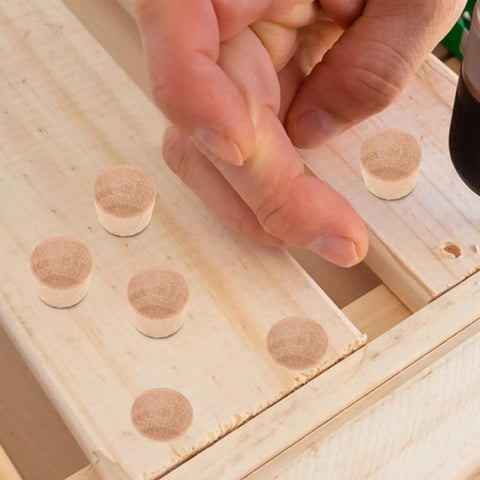 Hand placing 50 Pack DIY Wooden Hole Caps and Pocket Hole Plugs Hardwood Wood Plugs for Cabinets on wooden surface