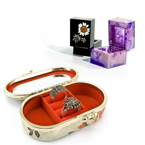 Open jewelry box with red velvet interior holding rings, floral and purple jewelry boxes in the background.