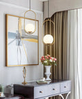 Modern One Light Globe Pendant With White Milk Glass Shade In Brushed Brass Finish For Kitchen Island Farmhouse Living Spaces Mid Century Style Ceiling Lighting Fixture in interior view next to artwork and flowers.