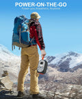 Hiker holding 99Wh Portable Power Station With LiFePO4 Battery, 120W Continuous Output, in mountain landscape.