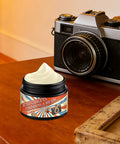 Phone Screen And Camera Lens Scratch Remover Paste 30ml jar next to vintage camera on wooden table