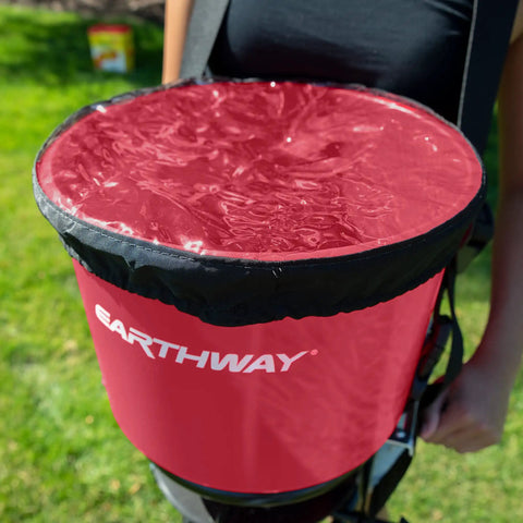 Close-up of Pro Grade Chest Mount Hand Crank Spreader with 40 lb hopper and rain cover, worn by a person on green lawn