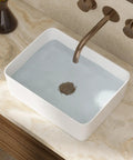 Rectangular white porcelain sink filled with water, mounted on marble counter with bronze wall-mounted faucet.