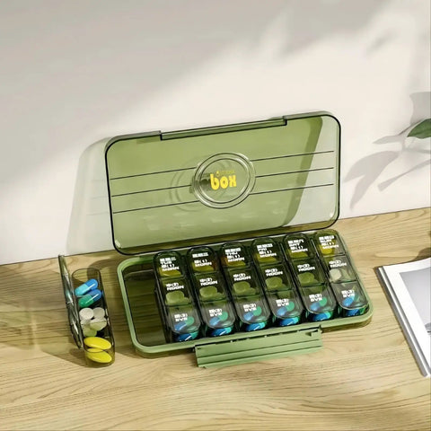 Green portable medicine organizer with individual compartments for pills, displayed open on a wooden table.