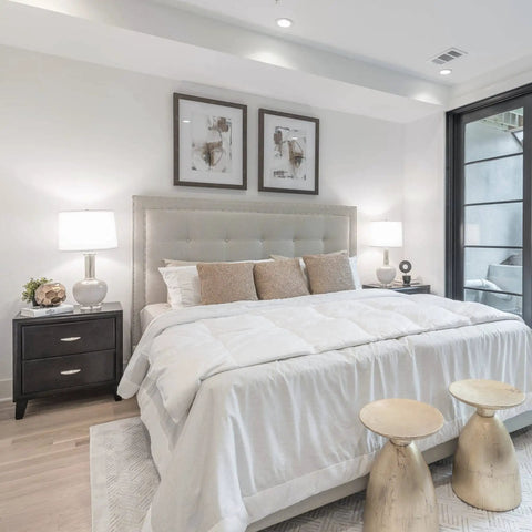 Modern bedroom with a king-sized bed, white comforter, bedside tables with lamps, two wall art pieces, and a sliding glass door.