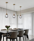 Smoked Glass Globe Pendant Light Brushed Gold Finish For Kitchen Island And Dining Room Dope Modern Mid Century Brass Hanging Fixture With A 7 Inch Shade And 13 Inch Height Perfect For Uplighting And Ambience illuminating dining area with modern furniture.
