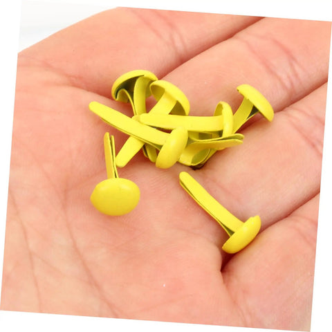 Hand holding yellow metal brads from 500 Pieces Scrapbooking Paper Fasteners Brads Clip Set For Photos And Cards And Paper Crafts Durable Vintage