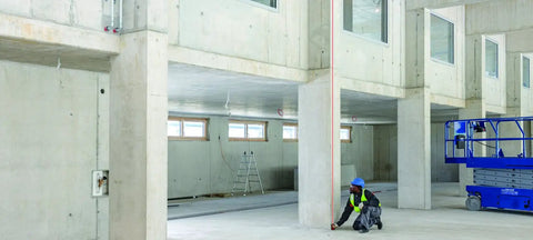 Person using Pro Grade Laser Distance Meter For Builders And DIYers With 200 Ft Range And 1.5 mm Accuracy in large indoor construction site.