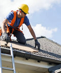 Person wearing safety gear installing roofing materials on a sloped roof with a ladder