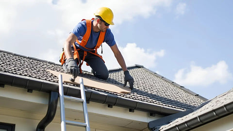 Person wearing safety gear installing roofing materials on a sloped roof with a ladder