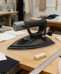 Heavy Duty Commercial Steam Iron Featuring Badass High Pressure Performance For Smooth Garment Pressing Factory Dry Cleaning And Bulletproof Temperature Control on a wooden table.