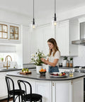 Kveosv 2 Pack Kitchen Island Pendant Lights, 8" Clear Glass Shade Black fixtures illuminating a modern kitchen with woman arranging flowers.