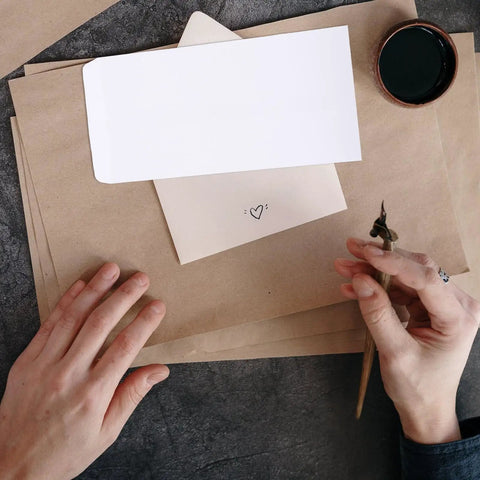 Person holding calligraphy pen near Thick White Blank Letter Envelopes 230x120mm Bulk Pack of 100 Durable Paper for Cash Envelopes Office Bill Storage and Mailing Supplies Easy Seal Clean Look for Everyday Mail on brown paper.