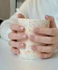 Hands holding a speckled mug showcasing pink cat eye glitter nails using Semi Cured Gel Nail Strips Kit With Cat Eye Glitter Pink Wraps