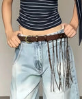 Dope Fringe Belt With Antique Bronze Buckle And Adjustable Waist Strap For Vintage Industrial Vibes And Edgy Streetwear Fits Dynamic Tassel Design Casual Accessory worn with light blue jeans.