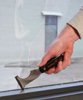 Person using Six In One Painter Tool for DIYers with scraper on window frame, featuring solvent resistant nylon handle and high carbon steel blade.